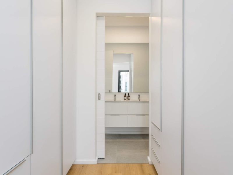 A clean, modern hallway featuring extensive built-in cabinetry and a sliding door leading into a contemporary bathroom with a vanity.