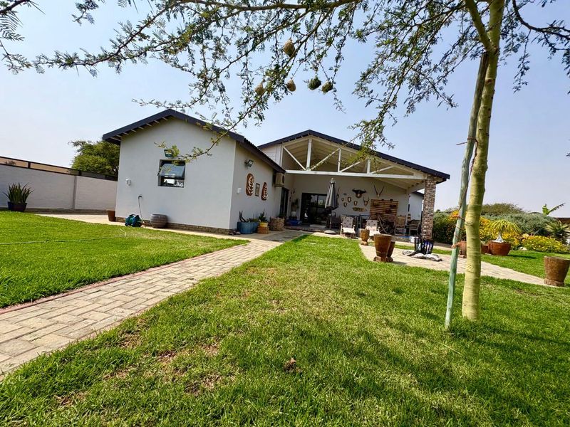 Rear view of the property featuring a covered patio with exposed roof trusses, brick paving, and a well-maintained lawn area.