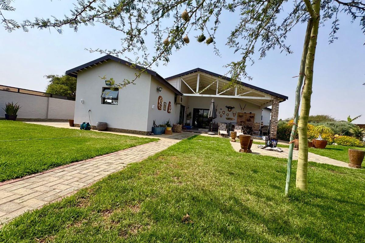 Rear view of the property featuring a covered patio with exposed roof trusses, brick paving, and a well-maintained lawn area.