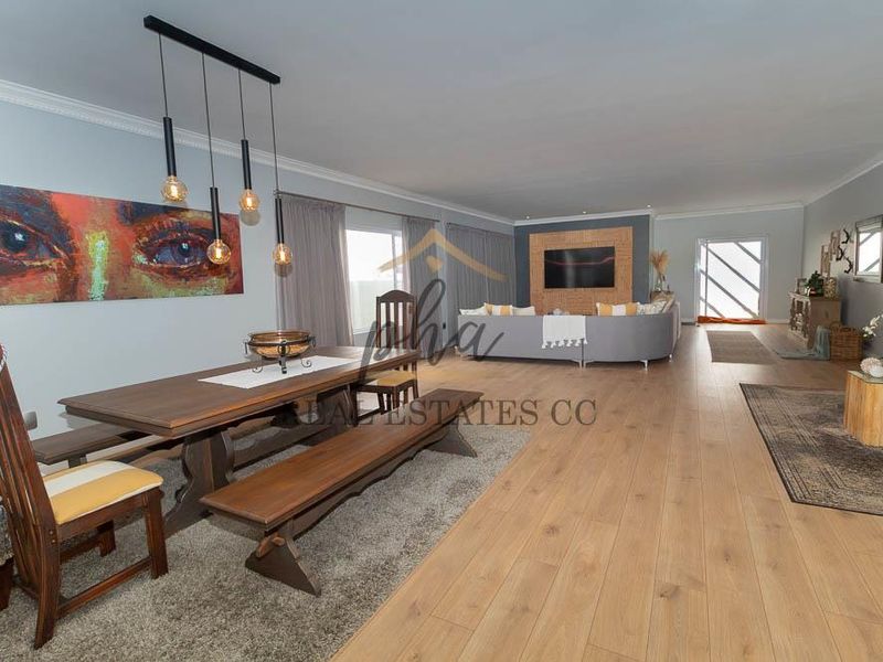 Spacious open-plan living and dining area featuring light laminate flooring, modern pendant lighting, and a custom built-in media wall.