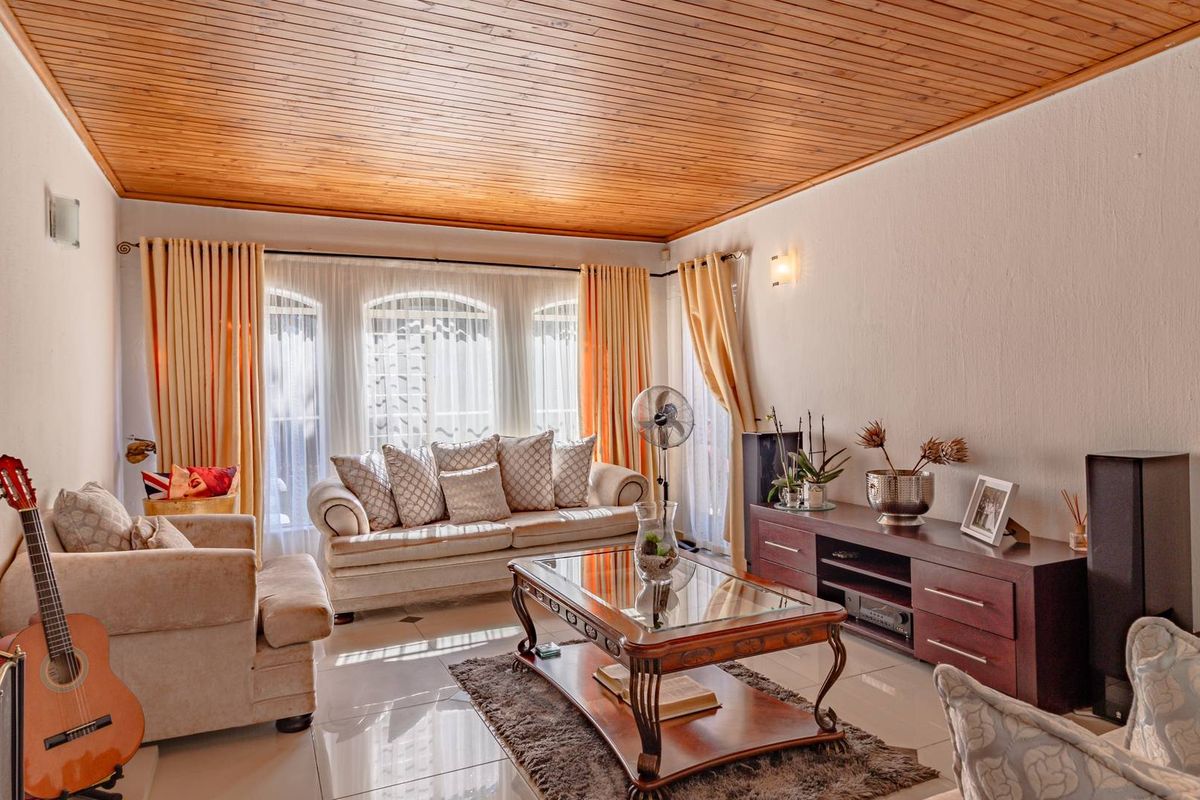 A comfortable living room featuring a warm timber-clad ceiling, large arch-top windows, and polished tiled flooring, creating a bright and inviting space.