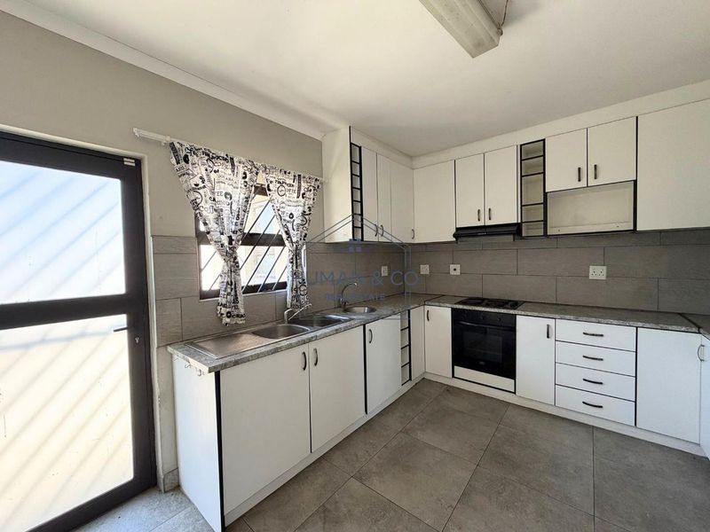A clean, functional kitchen featuring white cabinetry, a double sink, built-in oven, gas hob, and neutral tiled flooring with a tiled backsplash.
