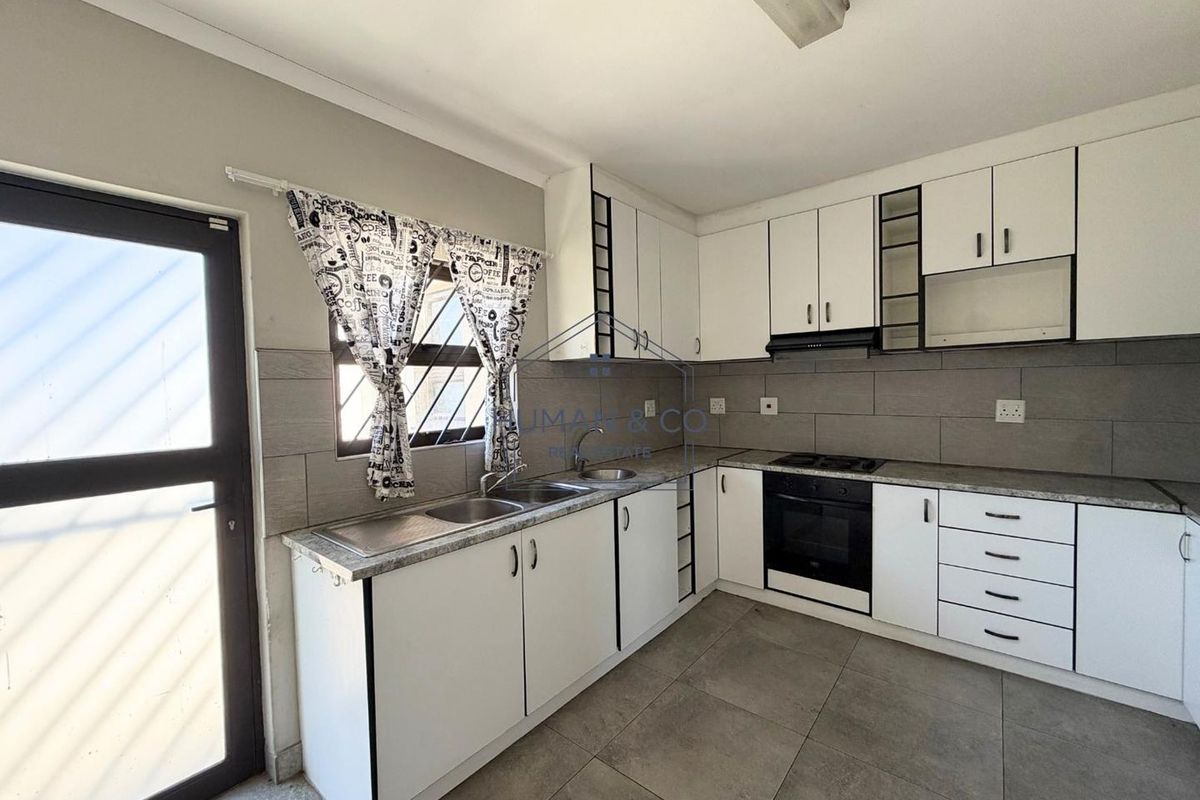 A clean, functional kitchen featuring white cabinetry, a double sink, built-in oven, gas hob, and neutral tiled flooring with a tiled backsplash.
