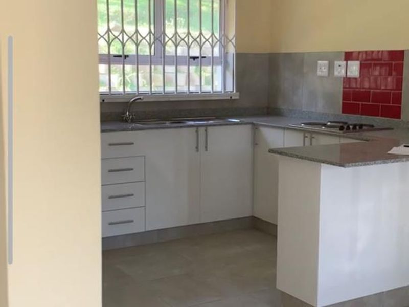 A functional, empty kitchen featuring white cabinetry, granite countertops, a built-in hob, and tiled splashbacks, ready for personalization.