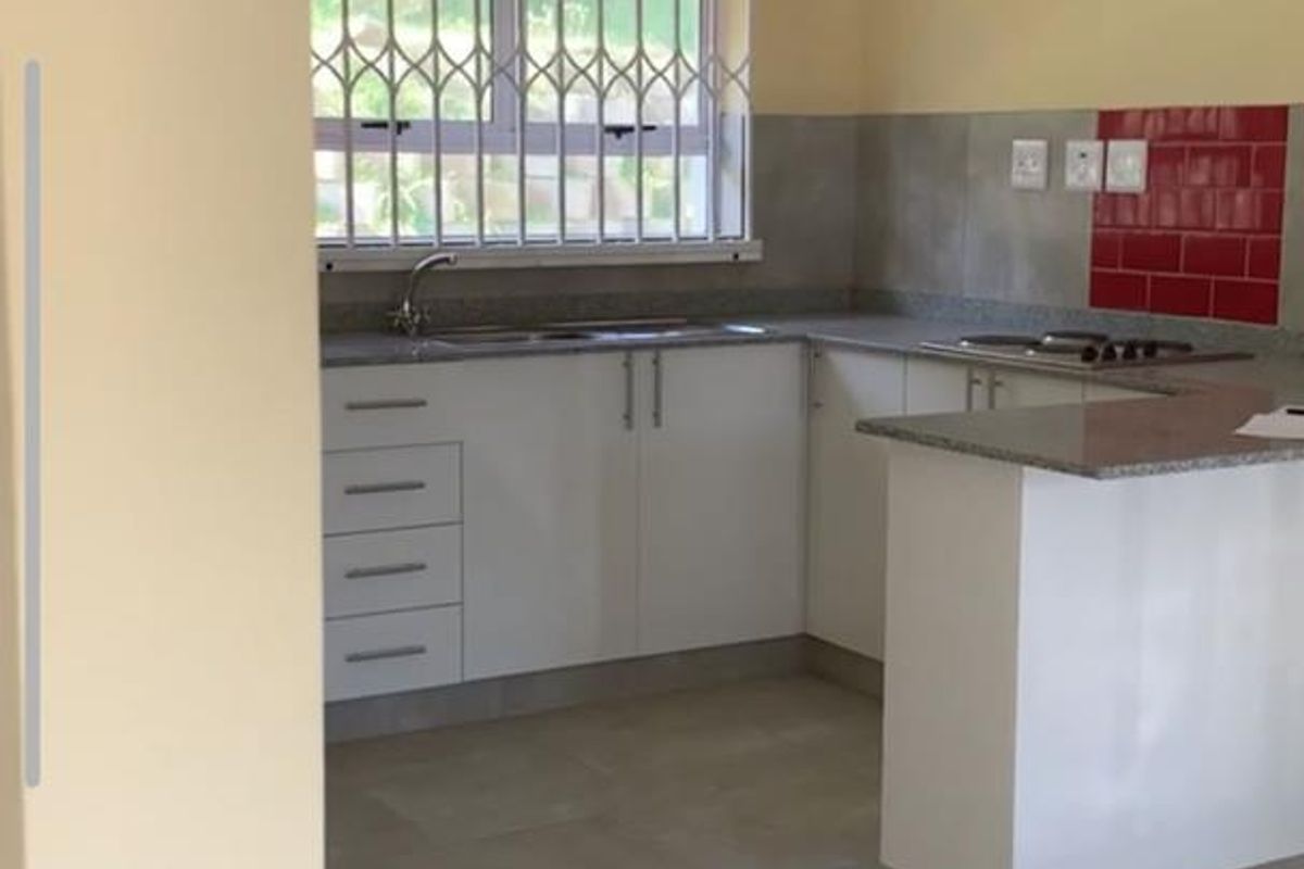 A functional, empty kitchen featuring white cabinetry, granite countertops, a built-in hob, and tiled splashbacks, ready for personalization.