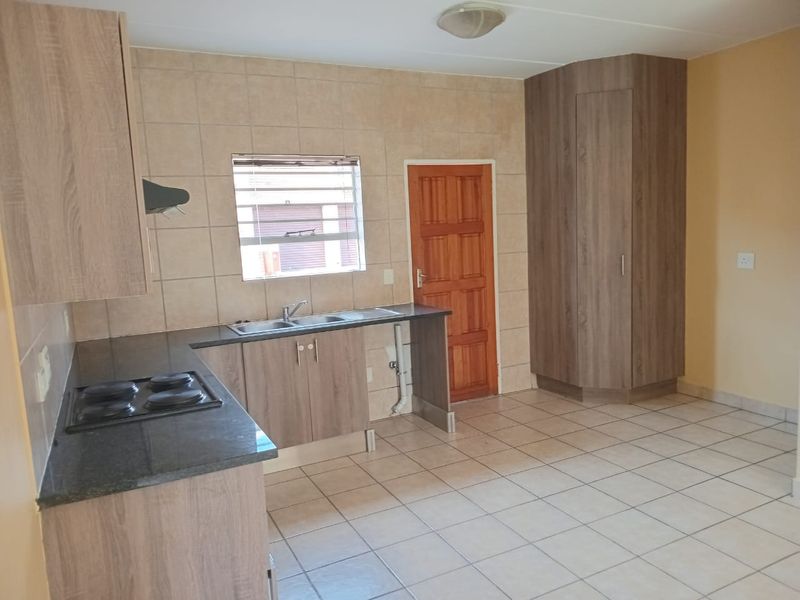A functional kitchen featuring wood-look cabinetry, dark countertops, a built-in hob, tiled backsplash, and ample storage space with a tall pantry cupboard.