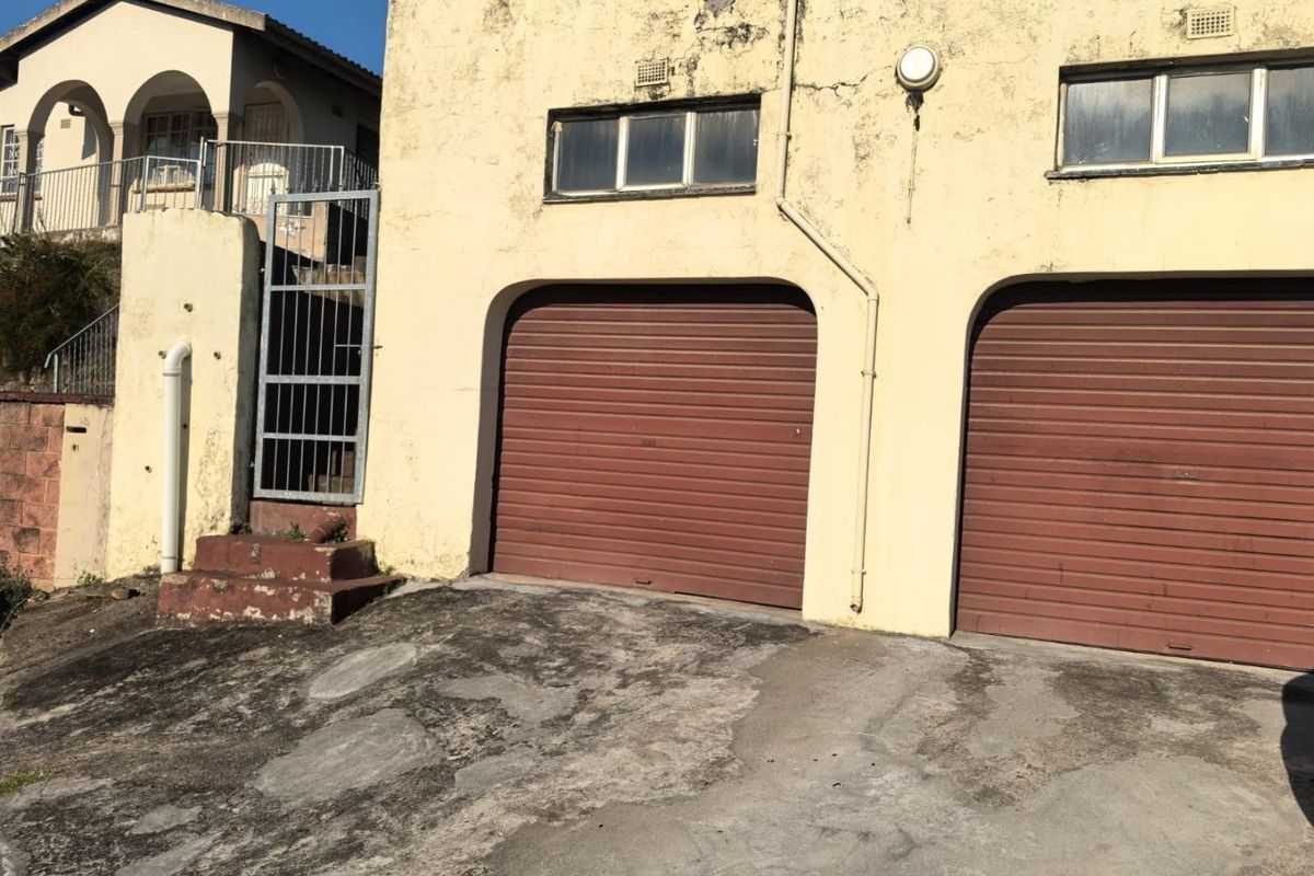 Exterior view of a double garage with roller doors and a concrete driveway, showing significant wear to the building facade and driveway surface.