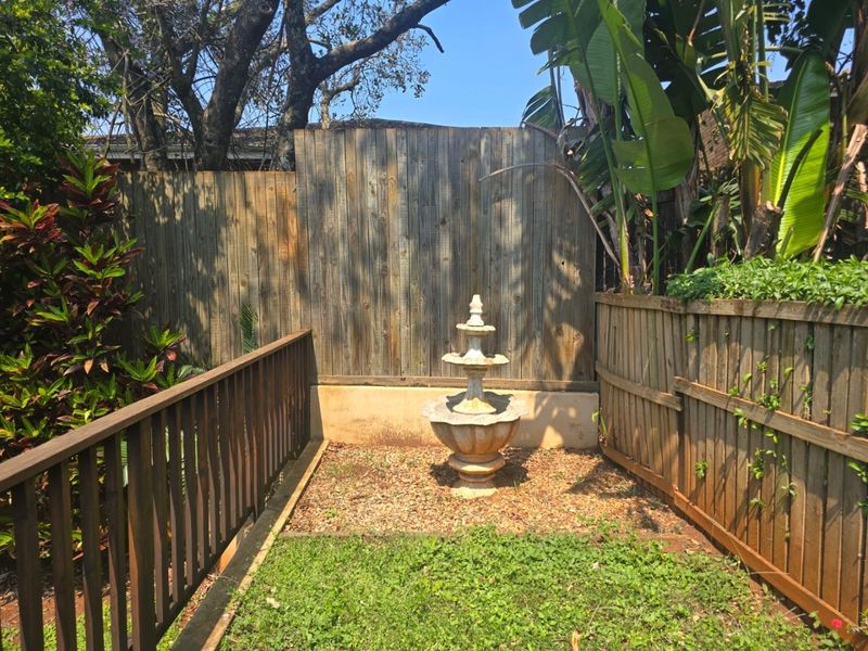 A private garden area featuring a central stone fountain, enclosed by timber fencing and mature landscaping.