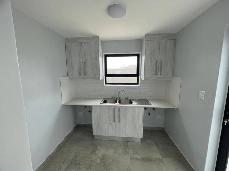 A clean, modern laundry room featuring light wood-grain cabinetry, a stainless steel sink, subway tile backsplash, and neutral floor tiles.