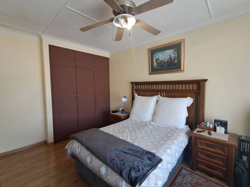 A bedroom featuring laminate flooring, a ceiling fan, and built-in cupboards with a dark finish.