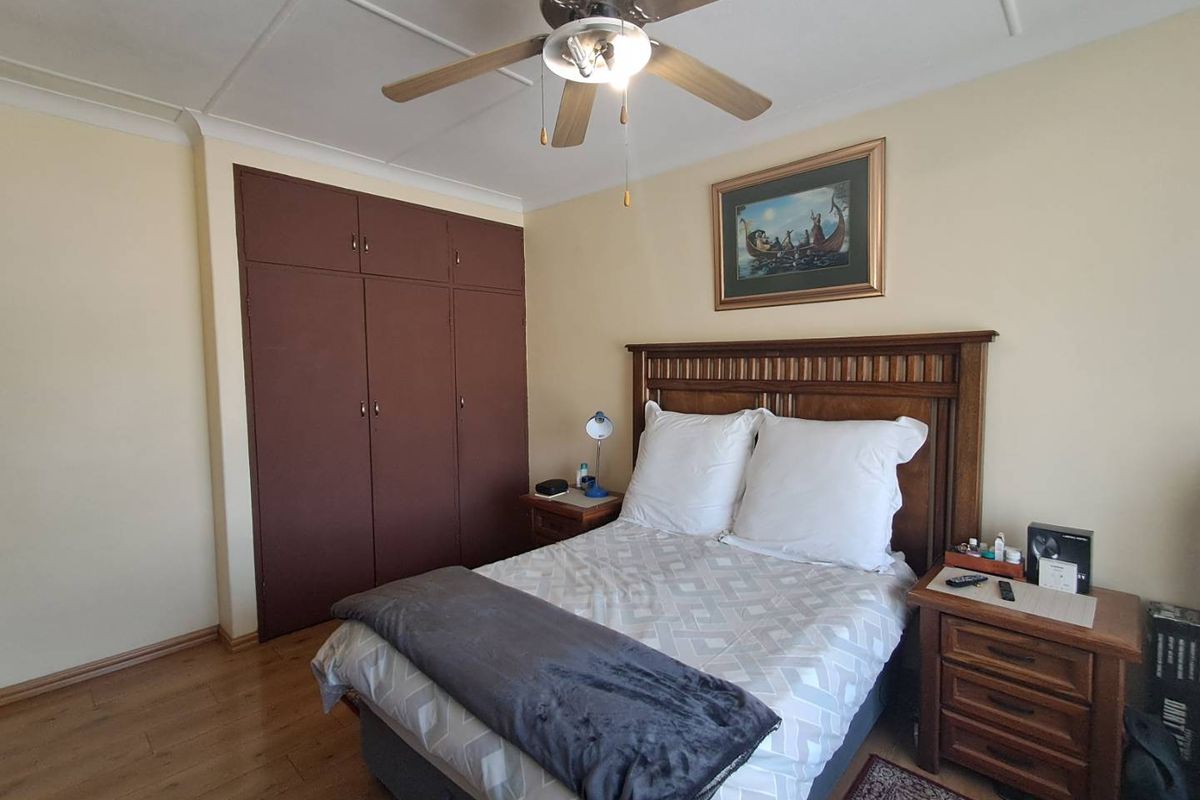 A bedroom featuring laminate flooring, a ceiling fan, and built-in cupboards with a dark finish.
