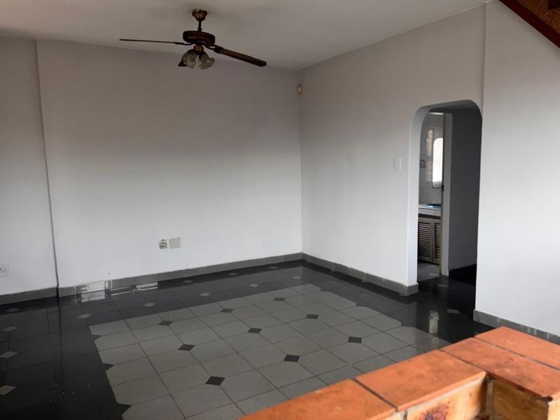 An empty living room featuring tiled flooring, a ceiling fan, and an arched doorway leading to an adjacent space.