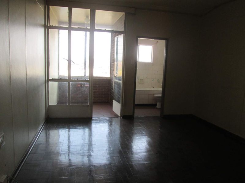 An empty bedroom featuring parquet flooring, direct access to a balcony, and an adjoining en-suite bathroom, offering a blank canvas for renovation.