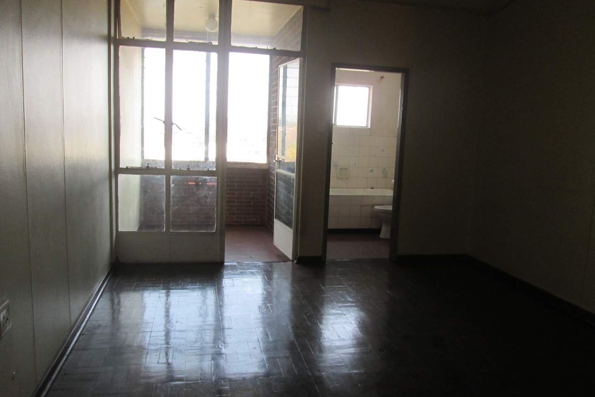An empty bedroom featuring parquet flooring, direct access to a balcony, and an adjoining en-suite bathroom, offering a blank canvas for renovation.