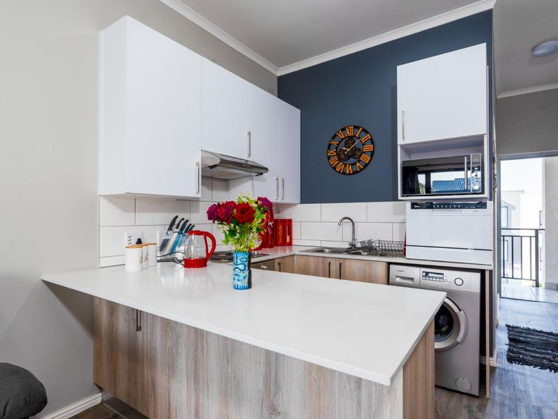Modern compact kitchen featuring white upper cabinetry, wood-finish lower cabinets, stone countertops, and integrated appliances, leading to a small balcony.