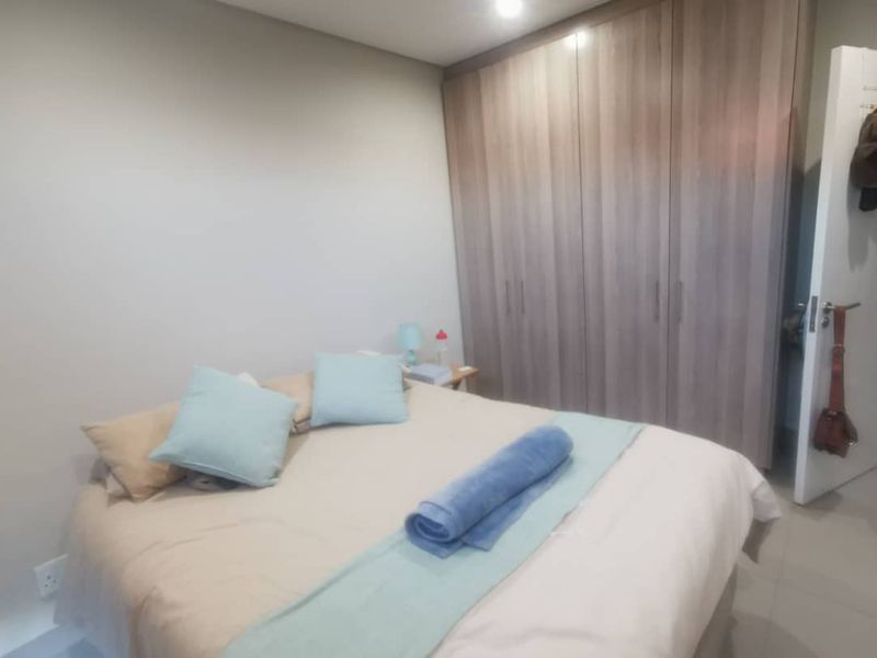 A well-maintained bedroom featuring neutral wall tones, tiled flooring, and extensive built-in wooden cupboards providing ample storage space.