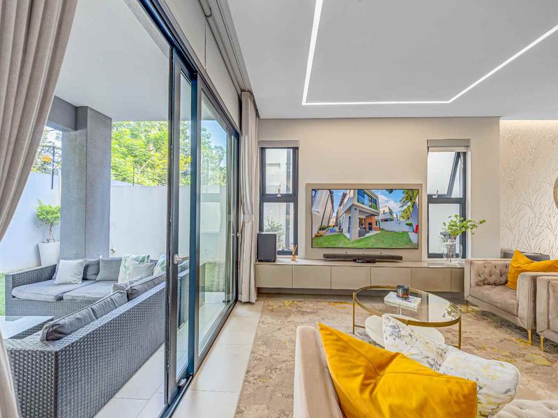 Modern living room featuring recessed LED lighting, large format floor tiles, and seamless access to the outdoor patio through expansive sliding glass doors.