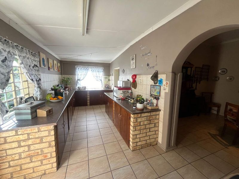 A dated kitchen featuring brick-based cabinetry, tiled splashbacks, and ceramic flooring, connected to an adjacent living area via a classic archway.