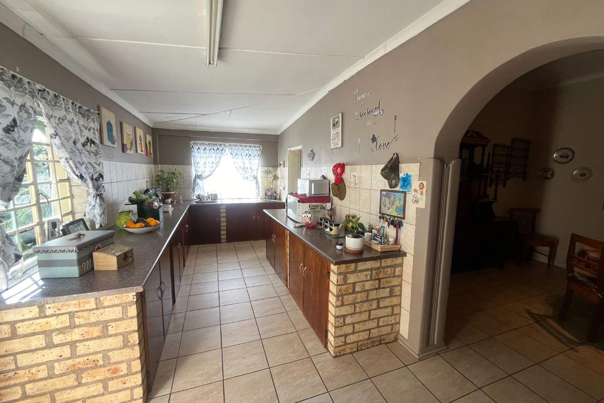 A dated kitchen featuring brick-based cabinetry, tiled splashbacks, and ceramic flooring, connected to an adjacent living area via a classic archway.