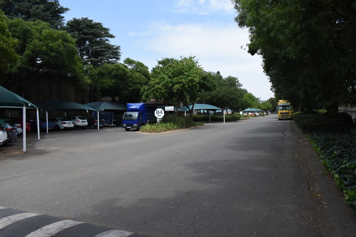 Outdoor parking area featuring covered shade-cloth parking bays and mature trees within an office park setting.