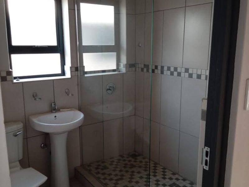 A clean, functional bathroom featuring a pedestal basin, toilet, and a walk-in shower with a glass screen and decorative tiled accents.