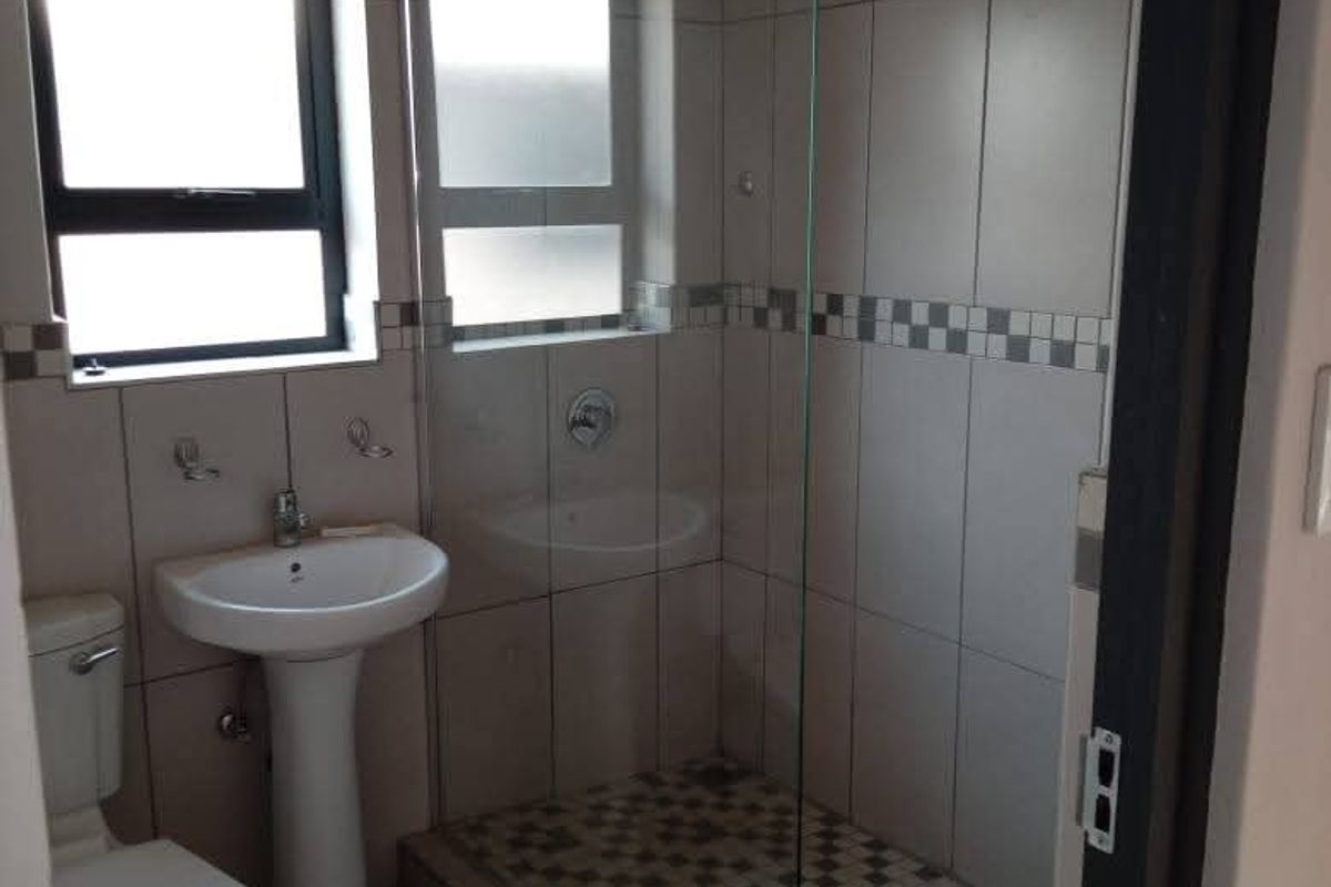 A clean, functional bathroom featuring a pedestal basin, toilet, and a walk-in shower with a glass screen and decorative tiled accents.
