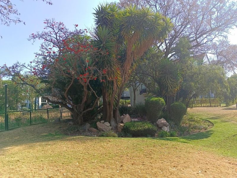 A well-maintained communal garden area featuring mature trees, landscaped shrubbery, and secure perimeter fencing within the apartment complex grounds.