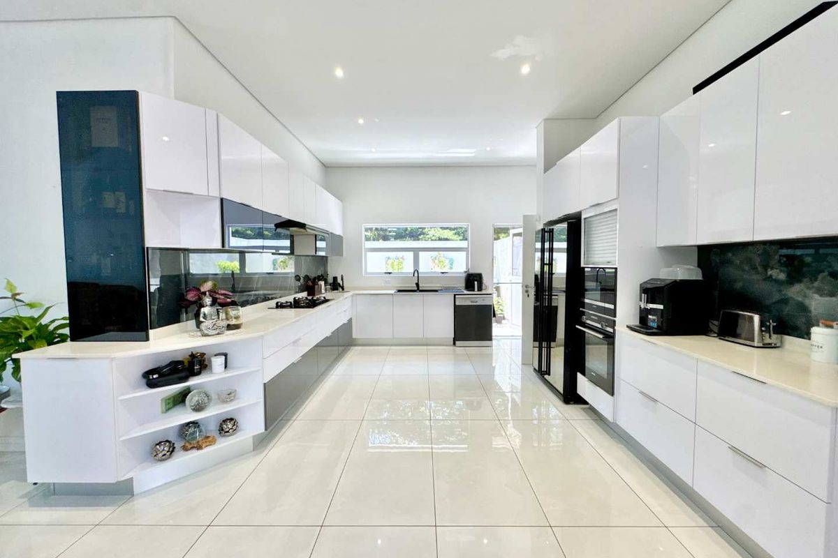 Modern, spacious kitchen featuring high-gloss cabinetry, integrated appliances, sleek countertops, and large-format floor tiles, offering a clean and contemporary aesthetic.