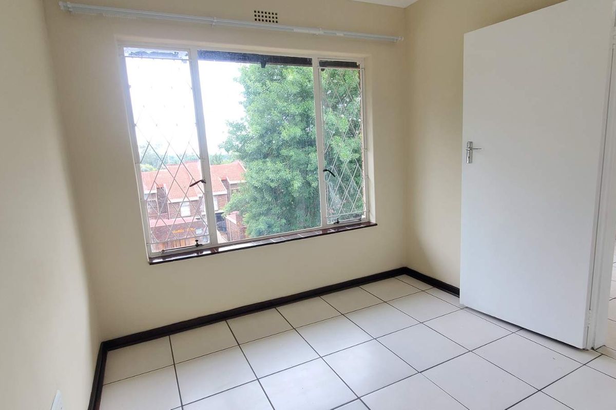 A bright, empty bedroom featuring tiled flooring, large windows with security bars, and a neutral color palette, ready for personalization.