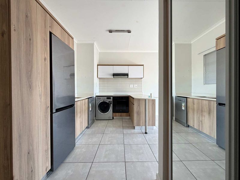 Modern kitchen featuring wood-look cabinetry, stone countertops, tiled flooring, and integrated appliance spaces, offering a clean and functional layout.