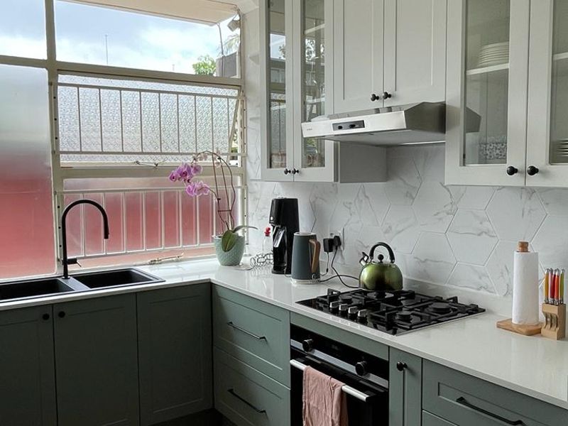 Modern kitchen featuring sage green lower cabinetry, white upper cabinets, quartz countertops, gas hob, built-in oven, and a stylish hexagon tile backsplash.