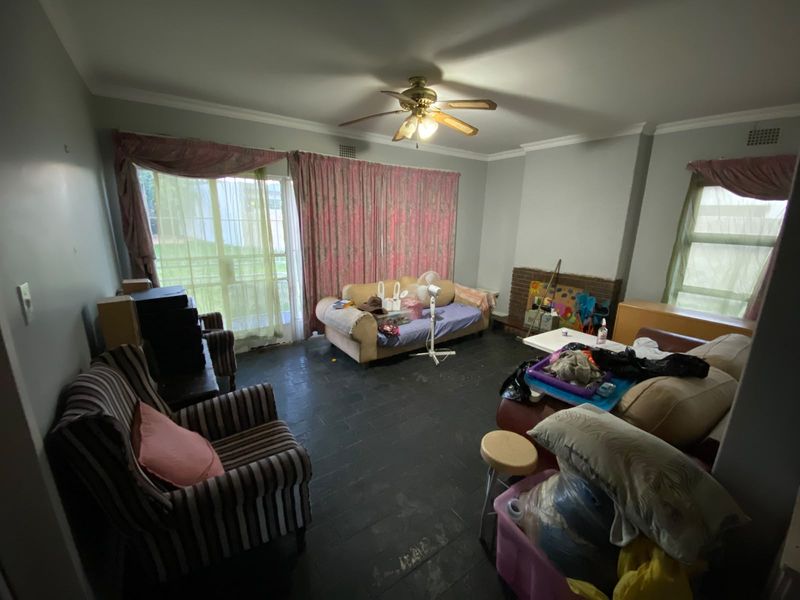 Spacious living room featuring a brick fireplace, ceiling fan, and sliding glass door access to the exterior, with dark tiled flooring throughout.