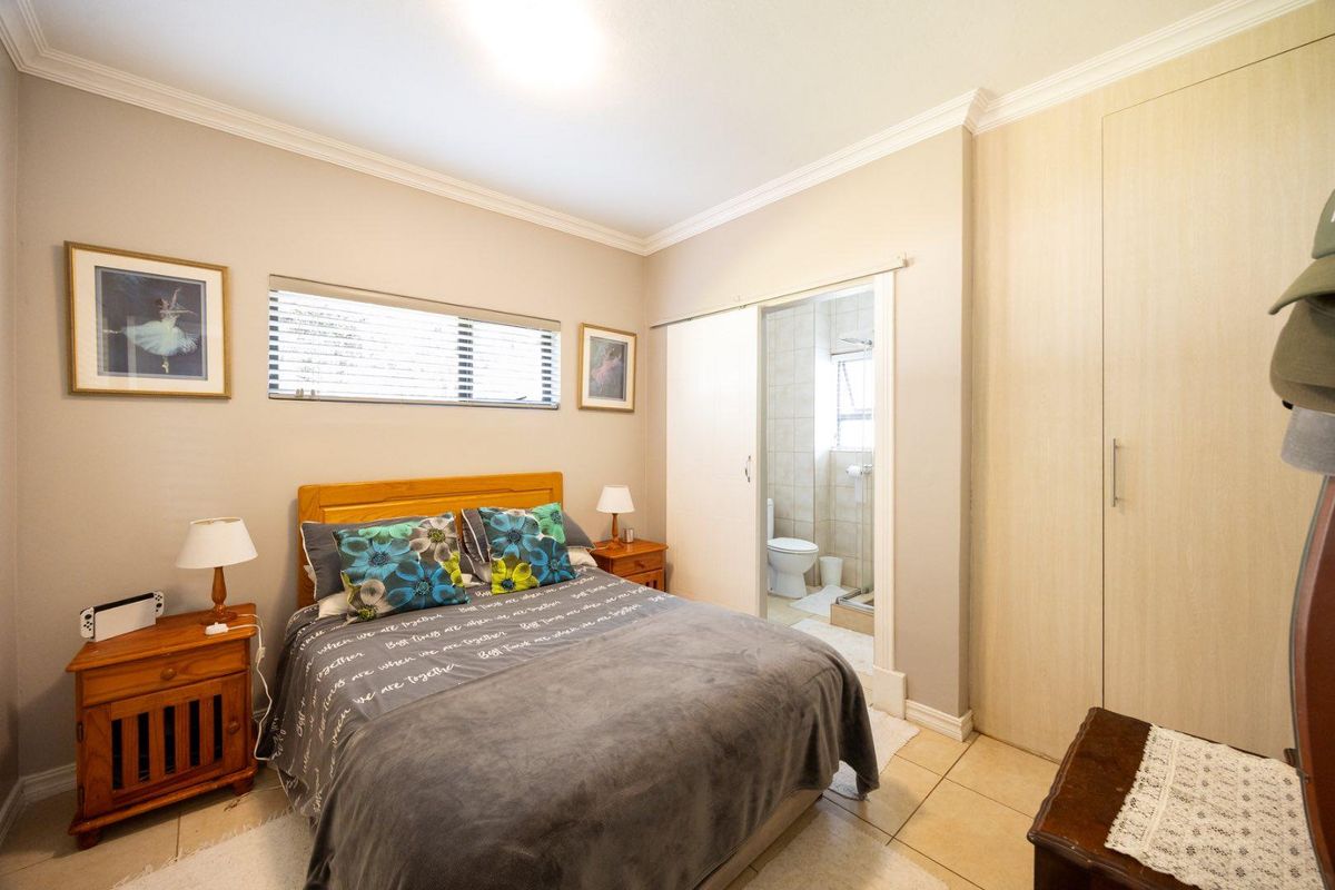 A well-maintained bedroom featuring built-in cupboards, tiled flooring, and an en-suite bathroom with a sliding door entry.