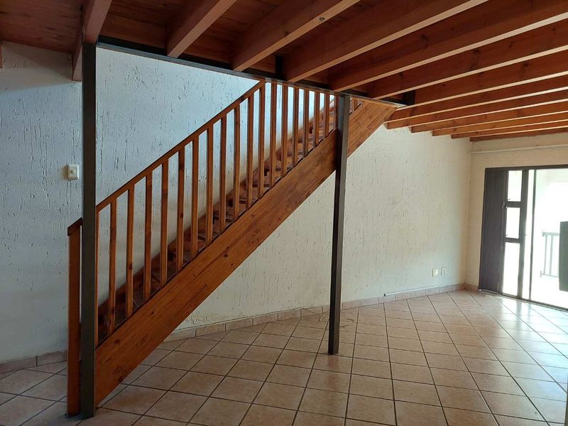 Open plan living area featuring exposed timber ceiling beams, a wooden staircase with balustrade, ceramic tiled flooring, and access to an outdoor area.