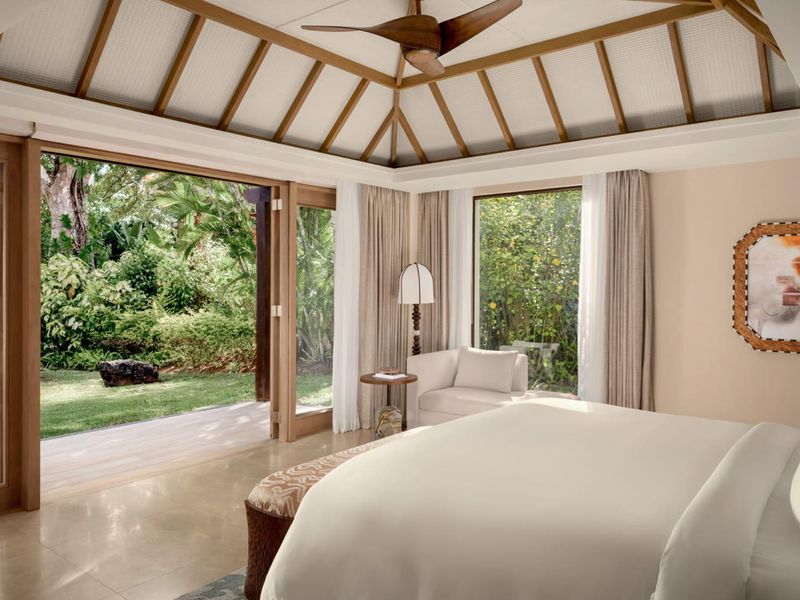 Spacious bedroom featuring a vaulted ceiling with exposed timber rafters, stone flooring, and large sliding glass doors opening onto a private garden terrace.