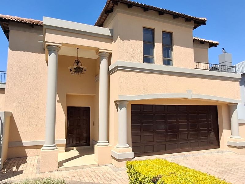 A well-maintained double-story home featuring a paved driveway, double garage, and a covered entrance with architectural columns.