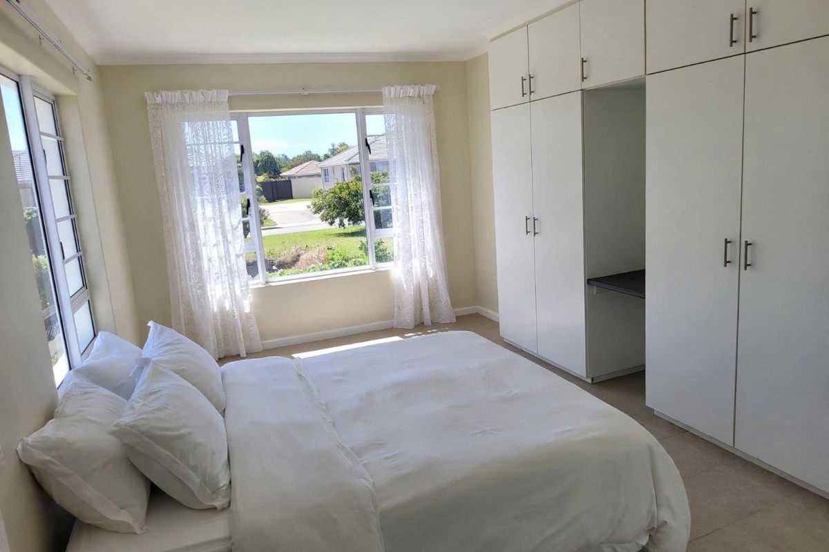 A bright bedroom featuring built-in cupboards with integrated desk space, tiled flooring, and large windows providing natural light.