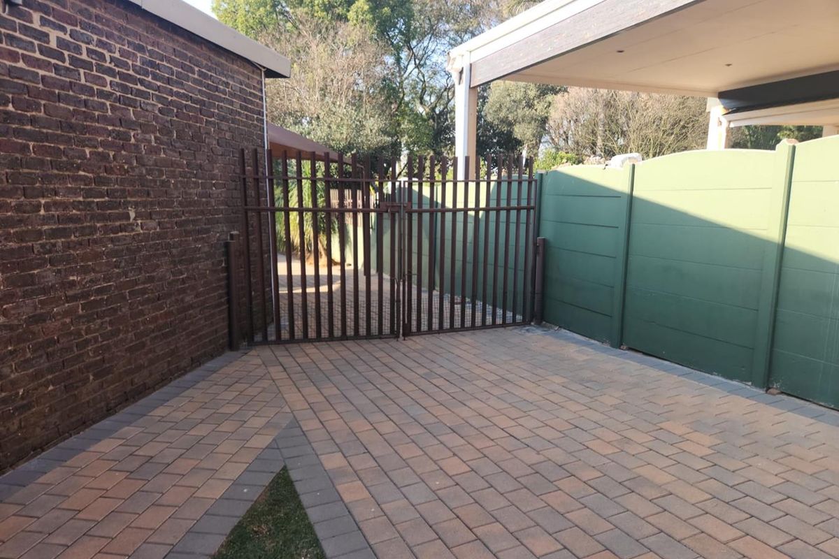 A paved rear courtyard area featuring a secure metal gate, brick walling, and a covered patio section.