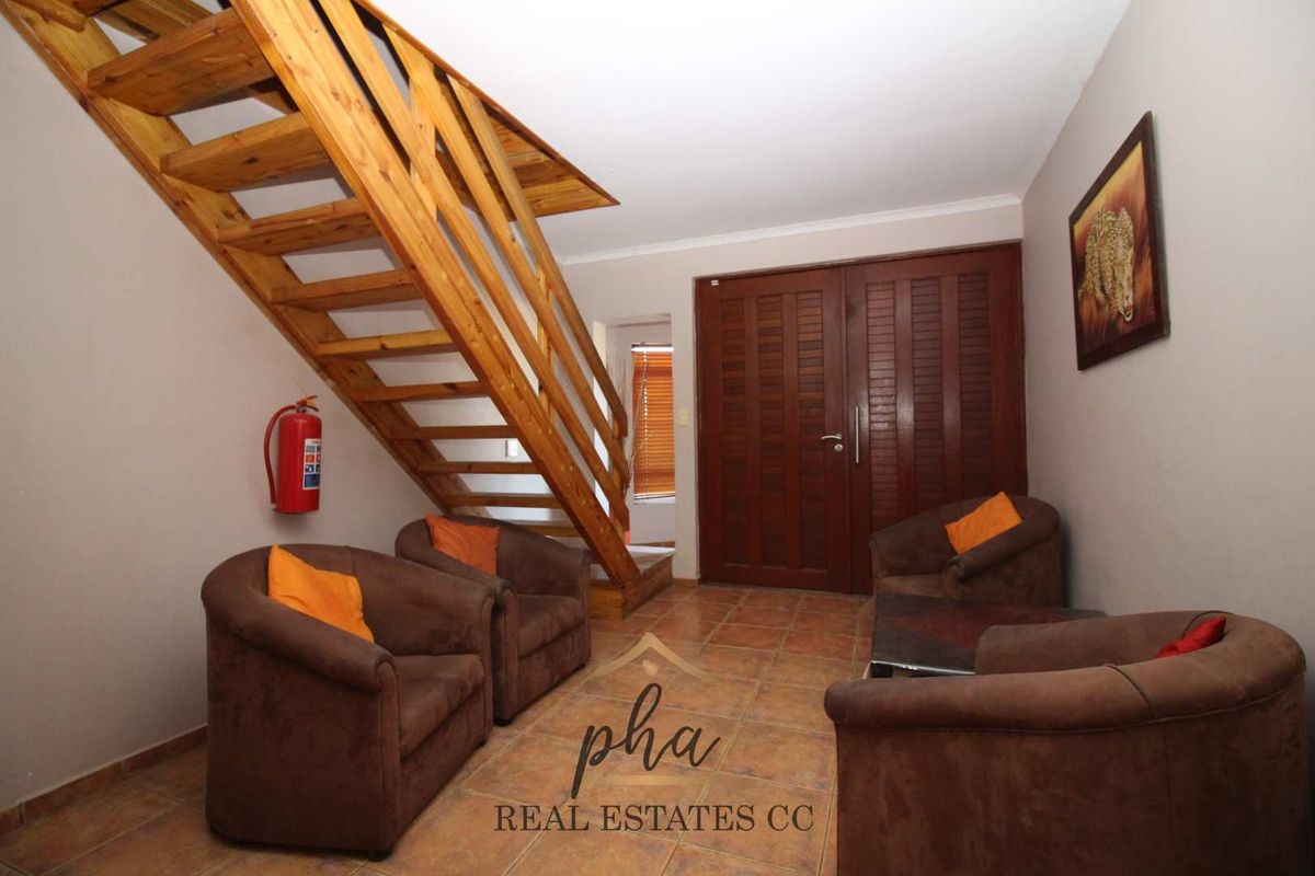 A living area featuring tiled flooring, a wooden staircase, and double wooden doors leading to an adjacent space.