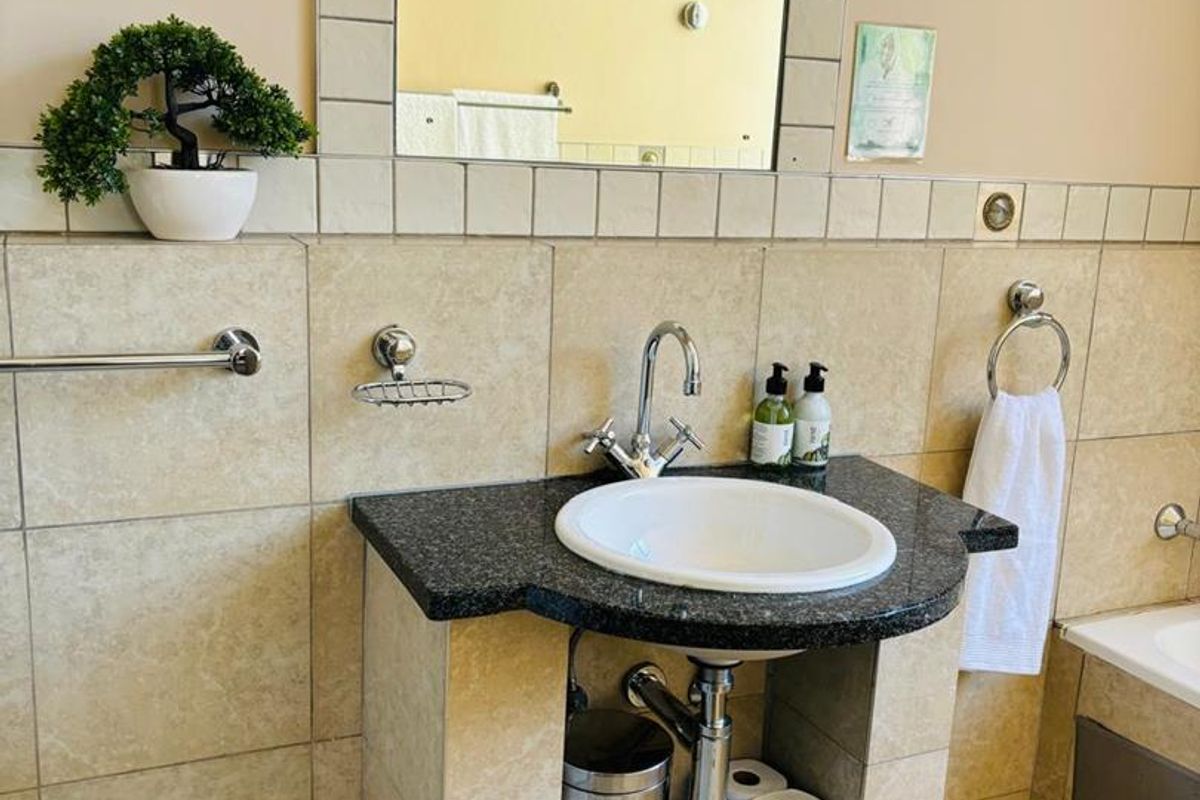 A bathroom vanity featuring a granite countertop, integrated basin, chrome faucet, and tiled splashback with a framed mirror.