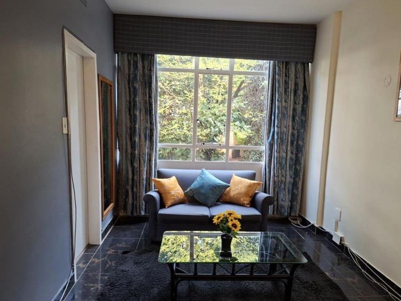 A cozy living room featuring dark tiled flooring and a large window that provides natural light and a view of the greenery outside.