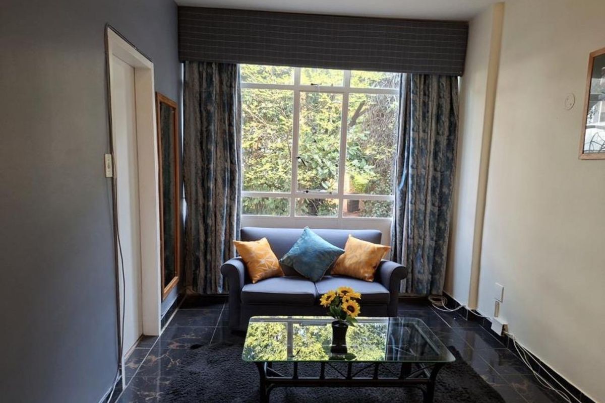 A cozy living room featuring dark tiled flooring and a large window that provides natural light and a view of the greenery outside.