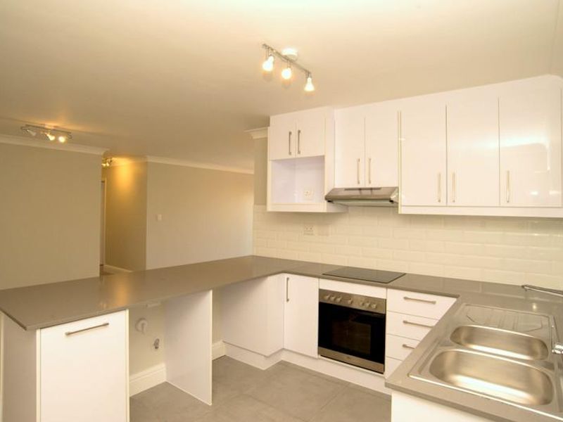 Modern open-plan kitchen featuring white gloss cabinetry, stone countertops, subway tile backsplash, and integrated appliances, seamlessly flowing into the adjacent living area.