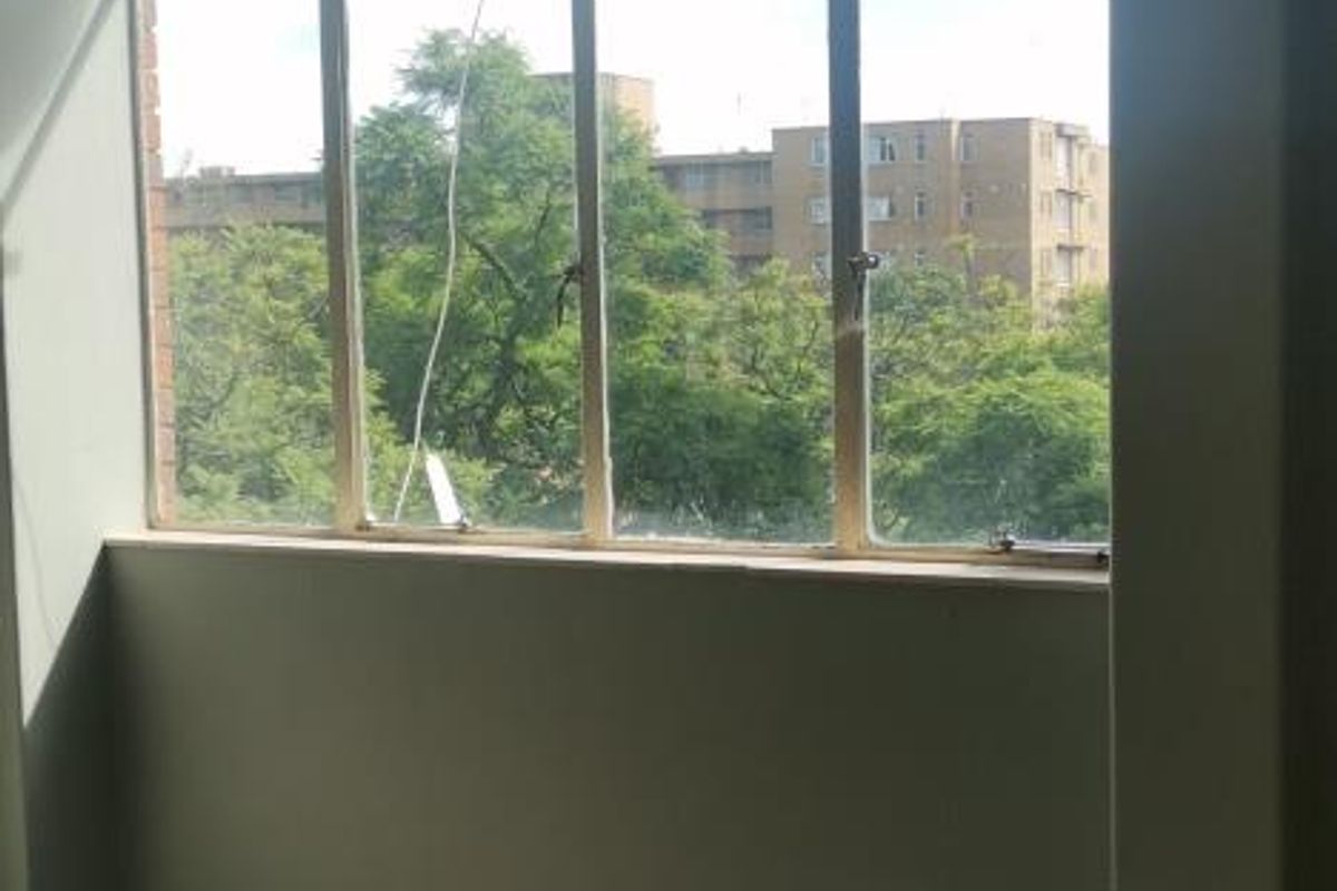 An empty living area featuring large windows with neighborhood views and worn vinyl tile flooring in need of repair or replacement.
