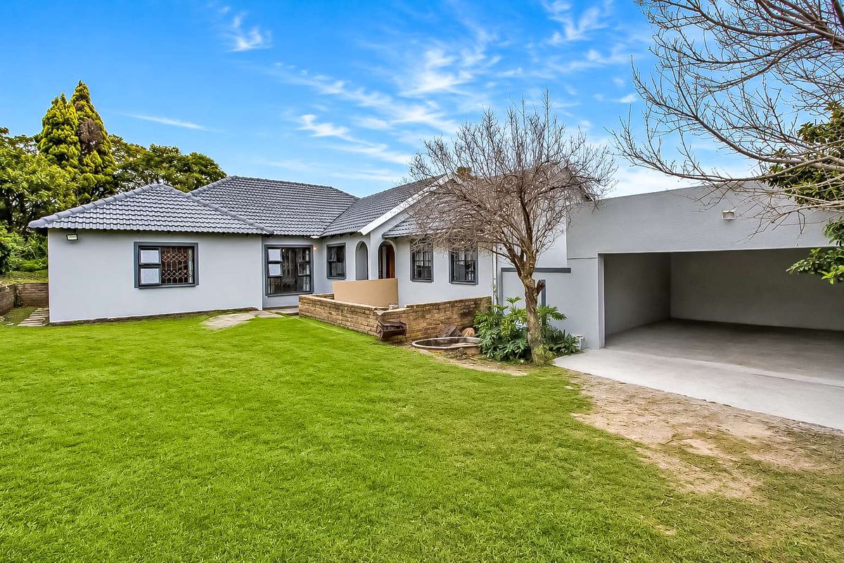 Rear view of the property featuring a spacious lawn, brick retaining wall, and an attached double garage with a concrete driveway.