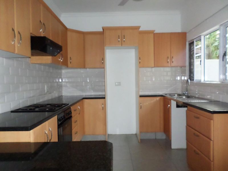 A functional kitchen featuring light wood cabinetry, dark granite countertops, a subway tile backsplash, and integrated cooking appliances.