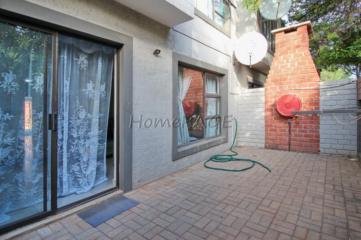 A paved rear patio area featuring a brick chimney structure, sliding glass door access, and exterior wall-mounted fire hose reel.