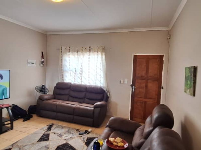 A functional living room featuring tiled flooring, a wooden entrance door, and cove cornicing, providing a neutral base for interior updates.