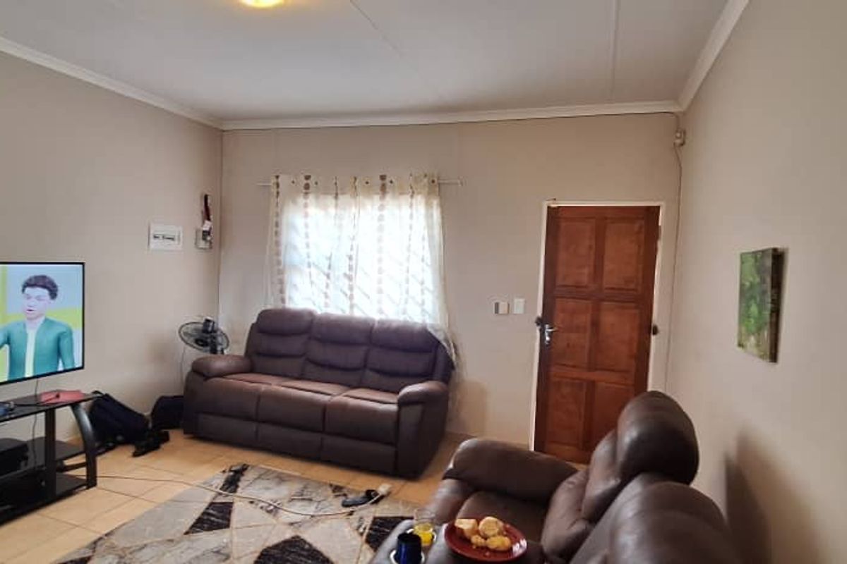 A functional living room featuring tiled flooring, a wooden entrance door, and cove cornicing, providing a neutral base for interior updates.