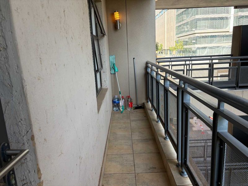 A narrow apartment balcony featuring tiled flooring, a metal safety balustrade, and a wall-mounted light fixture.